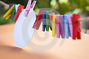Colorful background of wooden paper clips and white circle label paper on rope - on soft orange and green bokeh light background.
