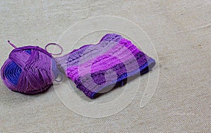 Colorful ball of wool and piece of woven winter garment with crochet needle or hook against light background. copy space