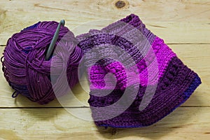 Colorful ball of wool and piece of woven winter garment with crochet needle or hook against light background. copy space