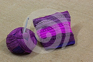 Colorful ball of wool and piece of woven winter garment with crochet needle or hook against light background. copy space