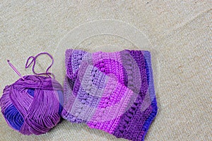 Colorful ball of wool and piece of woven winter garment with crochet needle or hook against light background. copy space