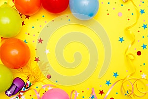 Colorful balloons and confetti on yellow table top view. Festive or party background. Flat lay style. Birthday greeting card.