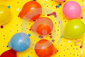 Colorful balloons and confetti on yellow table top view. Festive or party background. Flat lay style. Birthday greeting card.