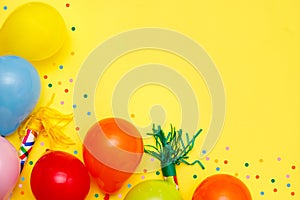 Colorful balloons and confetti on yellow table top view. Festive or party background. Flat lay style. Birthday greeting card.