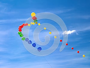Colorful balloons in a row floating in a light blue sky with clouds