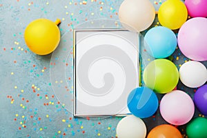 Colorful balloons, silver frame and confetti on blue table top view. Birthday or party mockup for planning. Flat lay style.