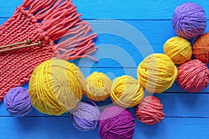 Colorful balls of wool, knitted scarf and knitting needles on blue rustic table
