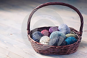 Colorful balls of wool yarn in a basket on the rustic background