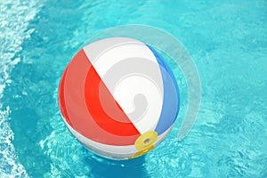 Colorful beach ball floating in swimming pool on sunny day