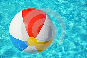 Colorful beach ball floating in swimming pool on sunny day