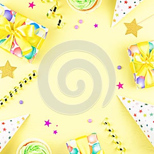 Colorful birthday party accessories on yellow. Wrapped gifts, confetti, balloons, party hats, decorations, copy space