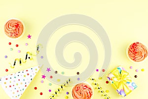 Colorful birthday party accessories on yellow. Wrapped gifts, confetti, balloons, party hats, decorations, copy space