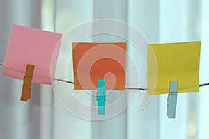 Colorful blank sticky notes hanging on natural wooden rope in pink, orange and yellow colors.
