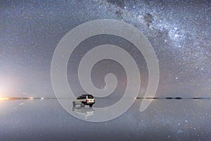 Colorful blue Milky way and bright starry night sky with reflections and a car on the Uyuni Salt Flats in Bolivia
