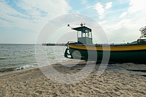 A colorful boat parked on the sandy beach in Gdynia, Poland. In the back there is a small pier going into the calm Baltic Sea