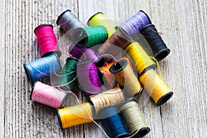 Colorful bobbins with sewing threads piled up on rustic wooden background