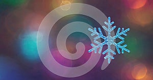 colorful, bokeh background. The snowflake exhibits intricate, symmetrical patterns and appears to be made of ice or crystal