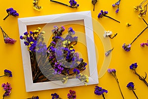 Colorful bouquet of dried autumn flowers lying on a white frame on yellow paper background. Copy space. Flat lay.