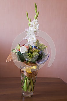Colorful bouquet with such flowers as gladiolus, orchid, roses, callas, mimosa are standing in the big glasses vase. Tints of whit