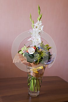 Colorful bouquet with such flowers as gladiolus, orchid, roses, callas, mimosa are standing in the big glasses vase. Tints of whit