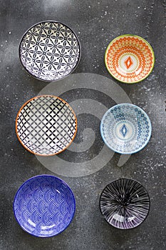 Colorful bowls on the black background, kitchen equipment on the table, bowl with geometric design.