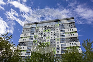 Colorful bright facade of a modern high-rise building with green trees against a blue sky with white clouds