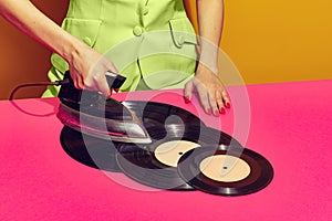Colorful bright image of woman using retro iron and ironing vintage vinyl records isolated over pink background.