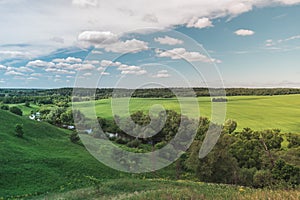 Colorful Bright Sunny Green Field Landscape With Blue Cloudy Sky, River Trees And Hills