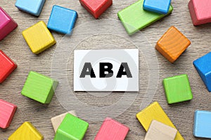 Colorful building blocks and card with abbreviation ABA on wooden table, flat lay