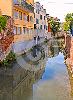 Colorful buildings, architecture, water reflections on city canal and old facade with blue sky in Padua Veneto, italy
