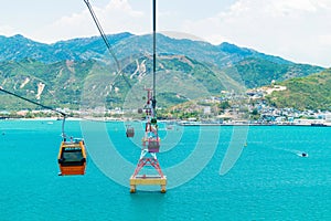 Colorful cabins of funicular over the sea with green mountains in the background and sandy shore