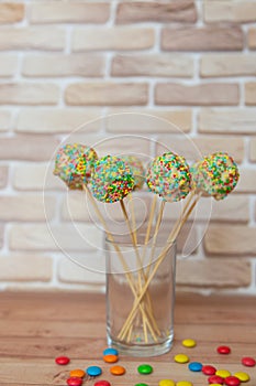 Colorful cake pops in tranparent glass in kitchen. Vertical photo, selective focus