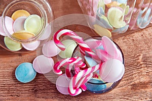 Colorful candies in jars on table on wooden background.Colorful candies spilling from a storage jar, old wood background.