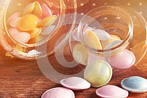 Colorful candies in jars on table on wooden background.Colorful candies spilling from a storage jar, old wood background.