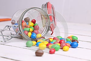 Colorful candles spilling out of a topple-over glass jar to a rustic wooden table