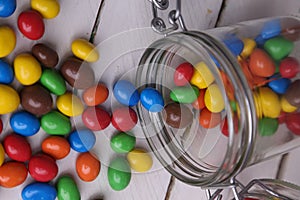 Colorful candles spilling out of a topple-over glass jar to a rustic wooden table