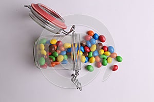 Colorful candles spilling out of a topple-over glass jar to a white table