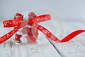 Colorful candy jar decorated with a red bow with hearts on white wooden background.