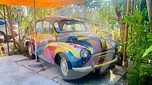 A colorful car is parked in front of a green bush