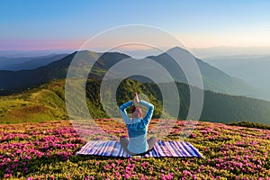 Colorful carpet. The yoga girl in the lotus pose. The lawn with the rhododendron flowers. High mountains. Meditation. Summer.