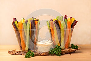 colorful carrots and cucumbers vegetables julienned in two plastic cups and sour cream dip with parsley over wooden