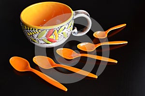 Colorful ceramic cup and orange teaspoons on a dark background