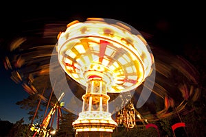 Colorful chain swing carousel in motion at amusement park at night.