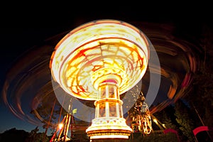 Colorful chain swing carousel in motion at amusement park at night.