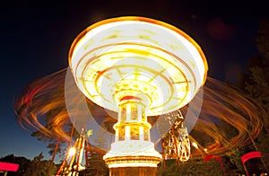 Colorful chain swing carousel in motion at amusement park at night.