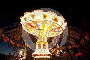 Colorful chain swing carousel in motion at amusement park at night.