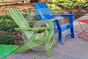 Colorful chairs on deck or patio in the back or front yard with green and blue seats on cement sidewalk in neighborhood