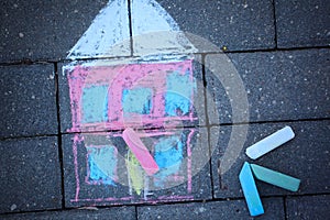 Colorful chalk drawing of house on acphalt surface.