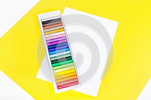 Colorful chalk pastels in box and sheet of white paper with space for text on yellow background