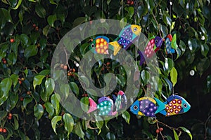 Colorful cheerful painted fish mobile hanging in a tree with red berries, spring and summer fun